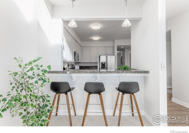 kitchen featuring a peninsula, hanging light fixtures, stainless steel refrigerator with ice dispenser, and a kitchen bar