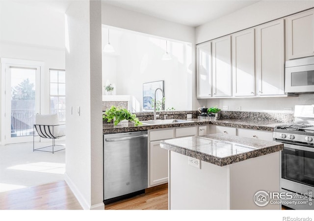 kitchen with tile counters, appliances with stainless steel finishes, white cabinets, a sink, and a kitchen island