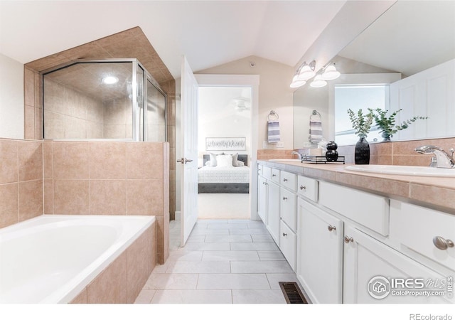 ensuite bathroom with a sink, visible vents, vaulted ceiling, a bath, and double vanity