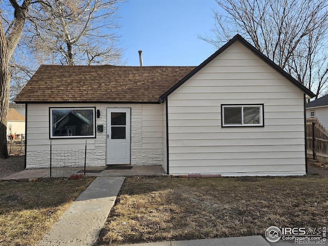 bungalow featuring stone siding, a shingled roof, fence, and a front lawn