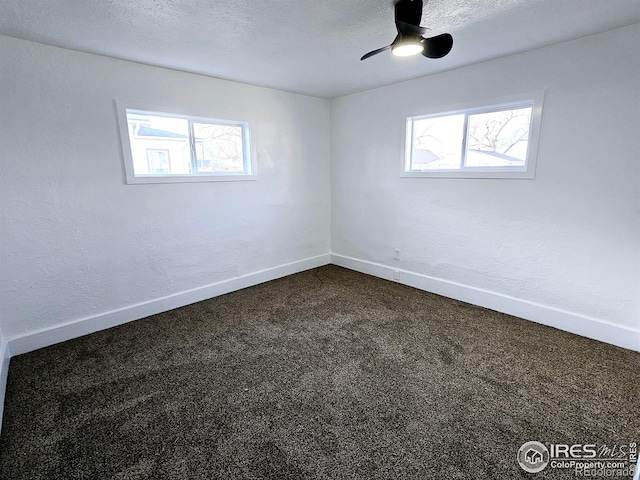 unfurnished room with a textured ceiling, dark colored carpet, a wealth of natural light, and baseboards