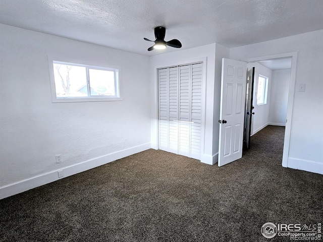 unfurnished bedroom featuring baseboards, a ceiling fan, dark colored carpet, a textured ceiling, and a closet