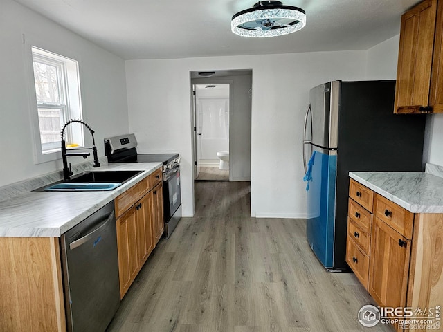 kitchen featuring stainless steel appliances, a sink, light countertops, and light wood-style floors