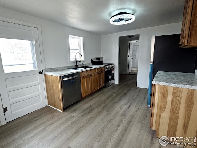 kitchen featuring light wood finished floors, light countertops, appliances with stainless steel finishes, and a sink