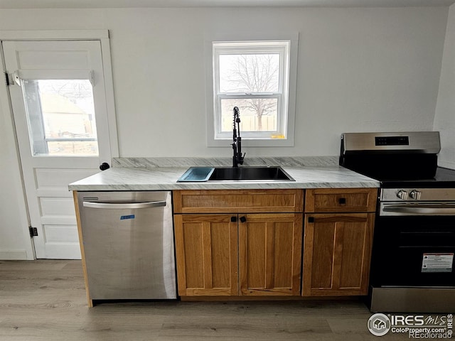 kitchen with brown cabinets, stainless steel appliances, light countertops, a sink, and light wood-type flooring