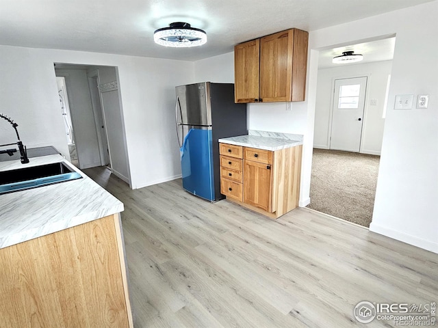 kitchen with light wood-style floors, a sink, freestanding refrigerator, and brown cabinets