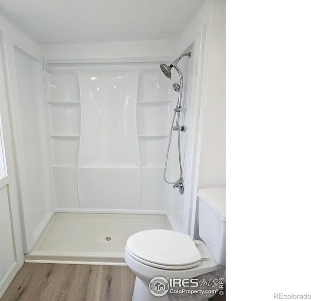 bathroom with a stall shower, toilet, and wood finished floors