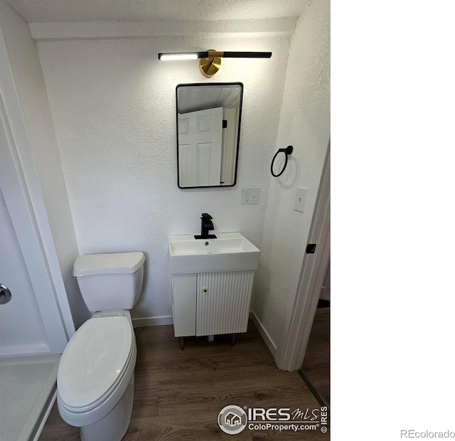 bathroom featuring a textured wall, toilet, wood finished floors, vanity, and baseboards