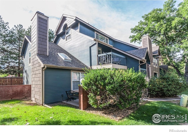 back of property featuring a chimney, a shingled roof, a patio area, fence, and a balcony