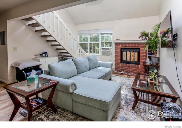 living area with stairs, a brick fireplace, wood finished floors, and electric panel