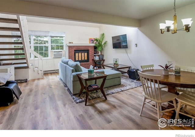 living area with wood finished floors, baseboard heating, stairway, a brick fireplace, and an inviting chandelier