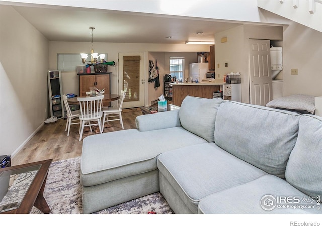 living room with baseboards, light wood finished floors, stacked washer / dryer, and a notable chandelier