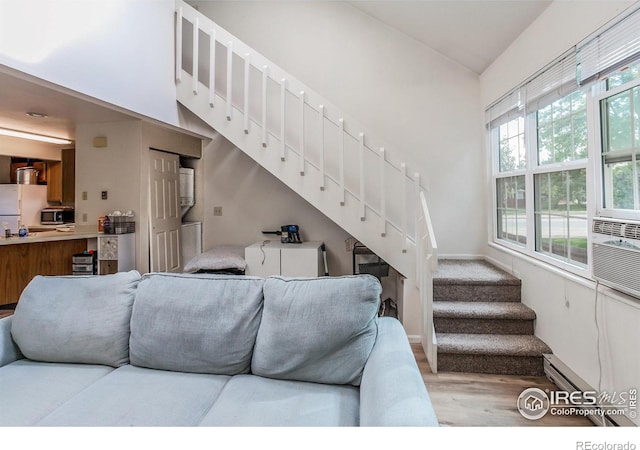 living area featuring a high ceiling, wood finished floors, baseboards, stairs, and baseboard heating