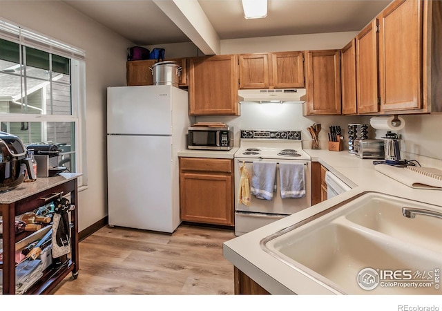 kitchen with light wood finished floors, light countertops, a sink, white appliances, and under cabinet range hood