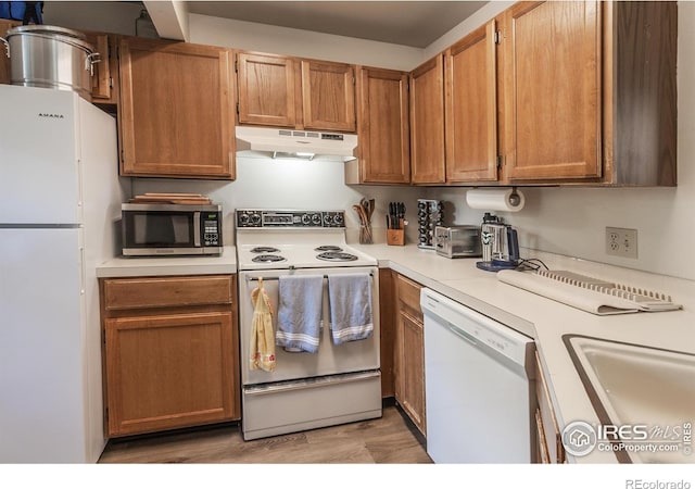 kitchen with light wood finished floors, light countertops, a sink, white appliances, and under cabinet range hood