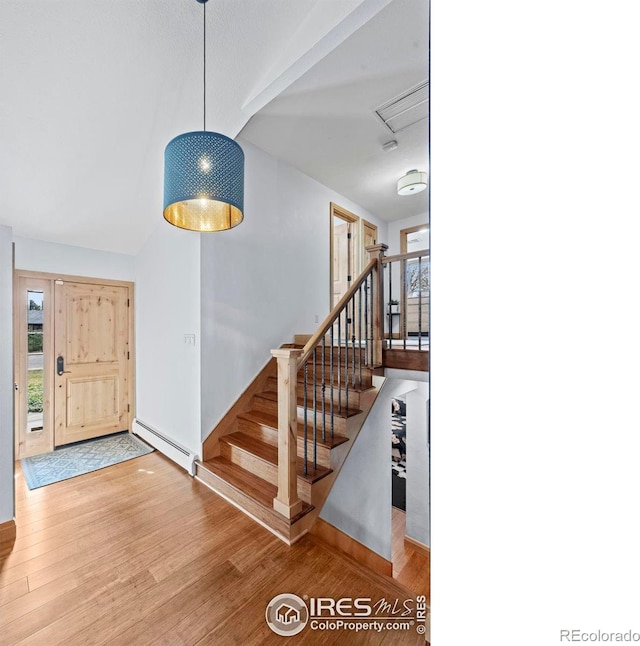 entryway featuring a baseboard heating unit, vaulted ceiling, stairs, and wood finished floors