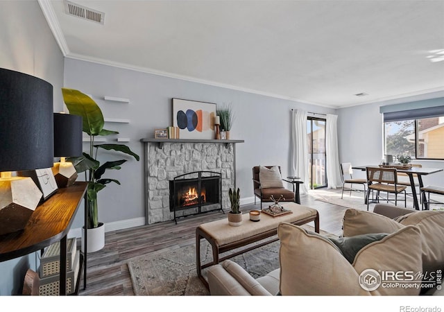 living room featuring baseboards, visible vents, ornamental molding, wood finished floors, and a fireplace