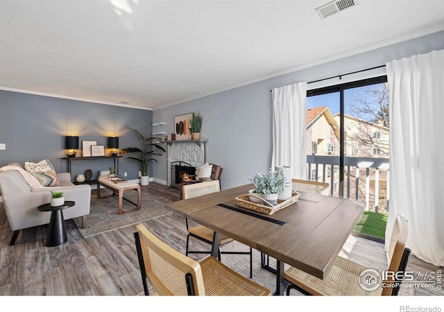 dining space with a fireplace, wood finished floors, visible vents, baseboards, and crown molding