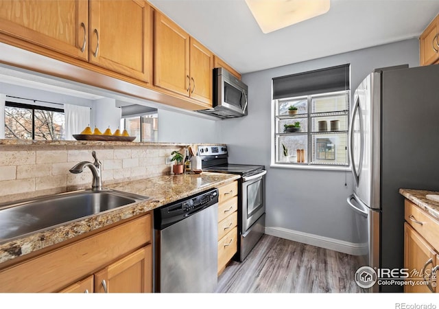 kitchen featuring light wood-style flooring, a sink, baseboards, appliances with stainless steel finishes, and backsplash