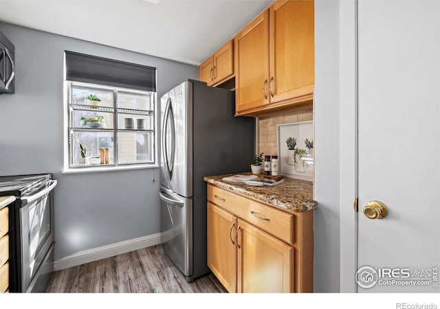 kitchen with baseboards, dark stone counters, appliances with stainless steel finishes, wood finished floors, and backsplash