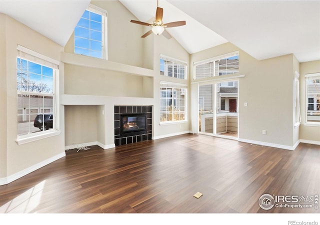 unfurnished living room featuring a tiled fireplace, baseboards, and wood finished floors