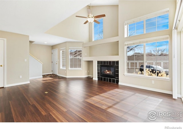 unfurnished living room featuring ceiling fan, a fireplace, wood finished floors, and baseboards