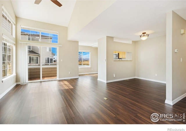 unfurnished living room featuring dark wood-style flooring, ceiling fan, a towering ceiling, and baseboards