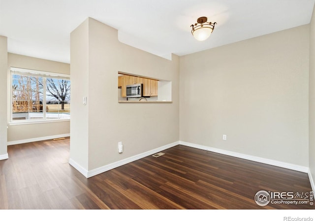 unfurnished room with dark wood-style floors, visible vents, and baseboards