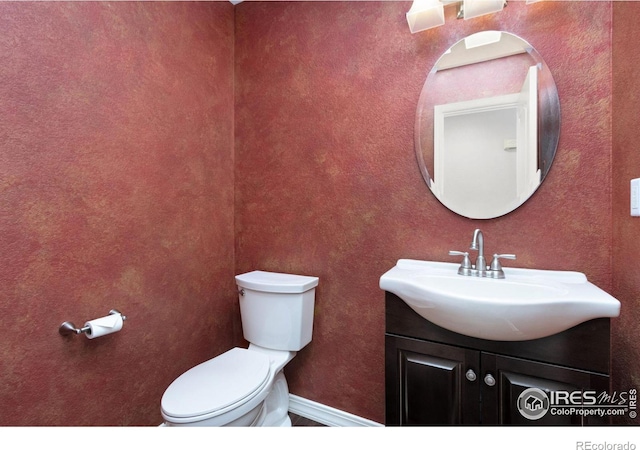 half bathroom with baseboards, vanity, and toilet