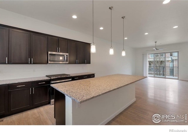 kitchen with light wood-style floors, a kitchen island, appliances with stainless steel finishes, and light stone counters