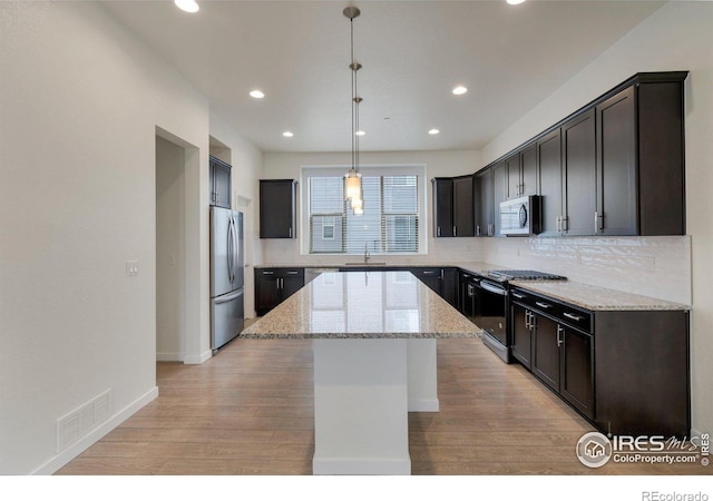 kitchen with light wood-style flooring, stainless steel appliances, a kitchen island, a sink, and visible vents