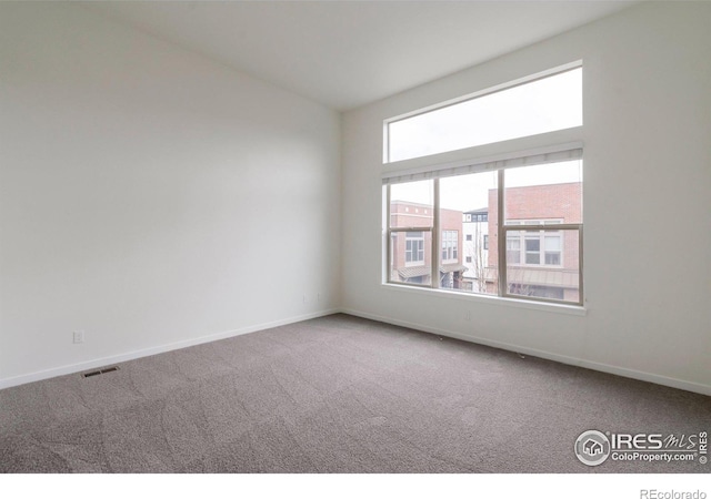 empty room with carpet flooring, visible vents, and baseboards