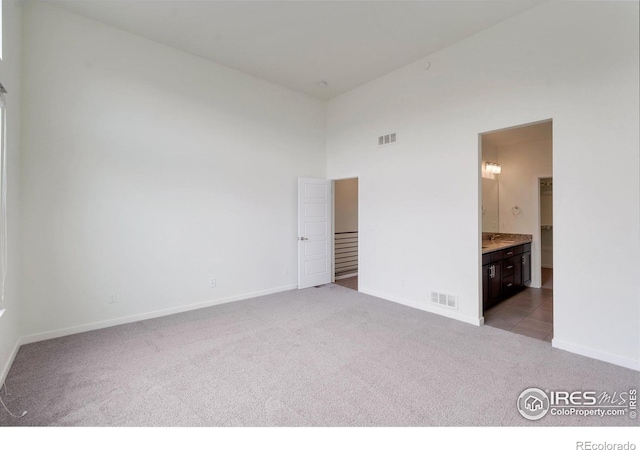 unfurnished bedroom with baseboards, visible vents, a towering ceiling, ensuite bath, and carpet floors