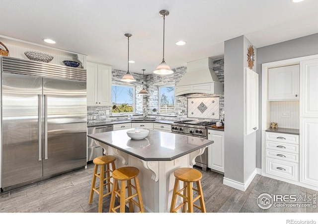 kitchen featuring high end appliances, premium range hood, dark countertops, a kitchen breakfast bar, and light wood-type flooring