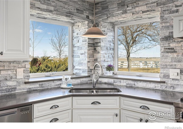 kitchen featuring dark countertops, decorative light fixtures, dishwasher, white cabinets, and a sink