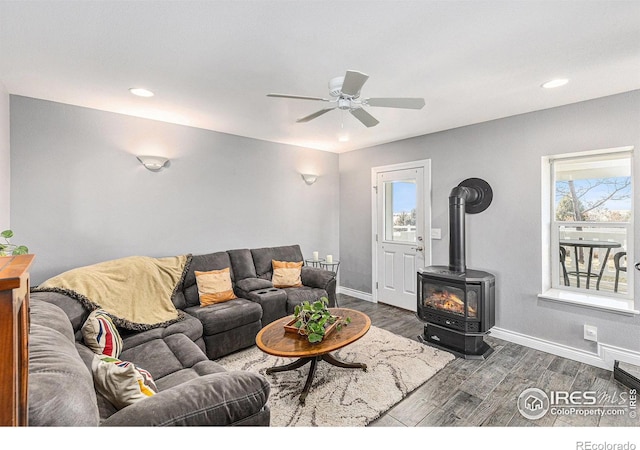 living area featuring ceiling fan, baseboards, wood finished floors, and a wood stove