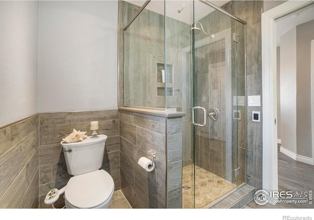 full bathroom with tile walls, toilet, and a stall shower