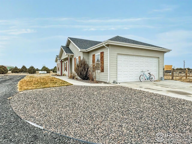 view of side of property with board and batten siding, roof with shingles, driveway, and a garage