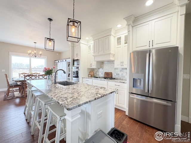 kitchen featuring a kitchen island with sink, stainless steel appliances, a sink, white cabinetry, and decorative backsplash