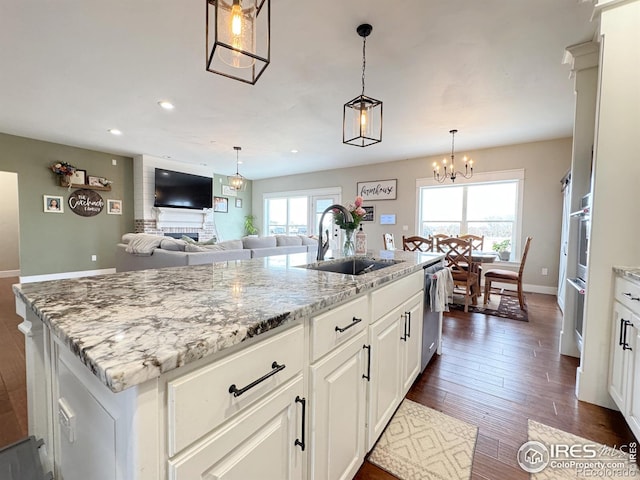 kitchen featuring dark wood-type flooring, a sink, an island with sink, light stone countertops, and dishwasher