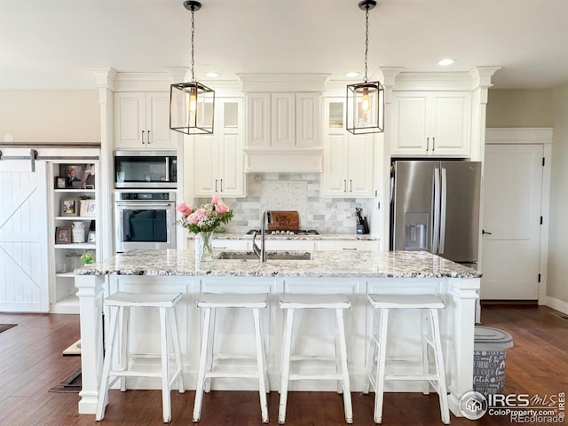 kitchen featuring a barn door, tasteful backsplash, an island with sink, appliances with stainless steel finishes, and light stone countertops