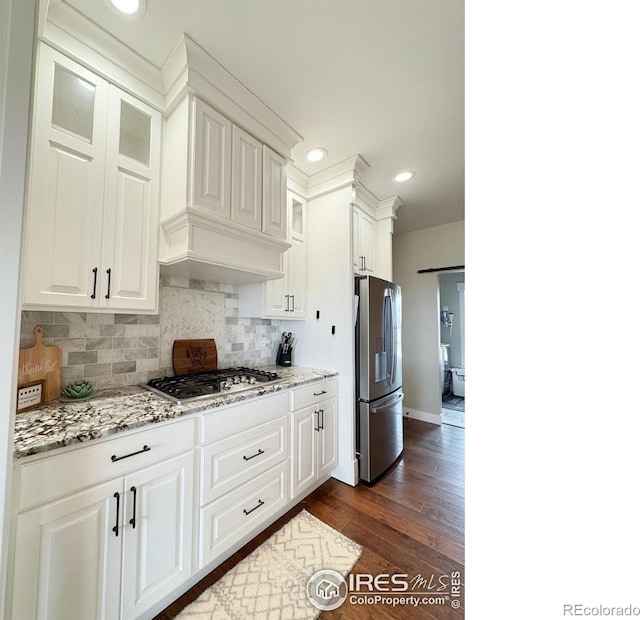 kitchen with appliances with stainless steel finishes, dark wood finished floors, glass insert cabinets, and decorative backsplash