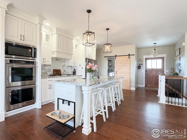 kitchen featuring appliances with stainless steel finishes, dark wood-style flooring, backsplash, and a barn door