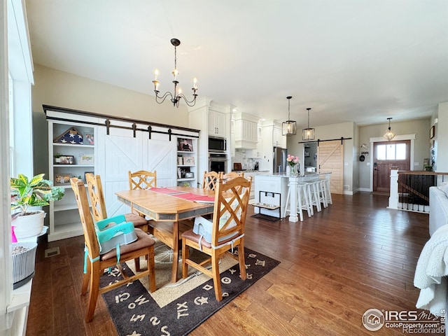 dining area with a barn door, visible vents, a chandelier, and dark wood-type flooring