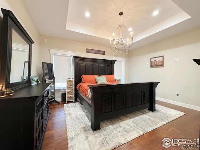 bedroom featuring a notable chandelier, recessed lighting, dark wood-type flooring, baseboards, and a raised ceiling