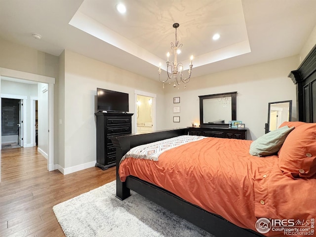 bedroom featuring a chandelier, a tray ceiling, baseboards, and wood finished floors