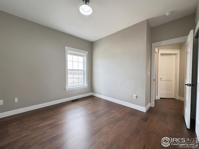 empty room with dark wood-type flooring, visible vents, and baseboards