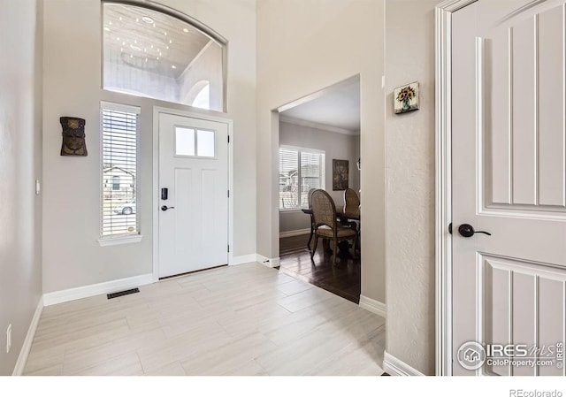 entrance foyer with ornamental molding, a high ceiling, visible vents, and baseboards