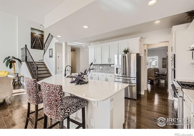 kitchen featuring stainless steel appliances, dark wood-type flooring, a kitchen bar, and decorative backsplash