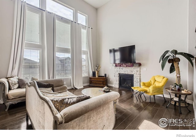 living area with a stone fireplace, dark wood-type flooring, and a high ceiling